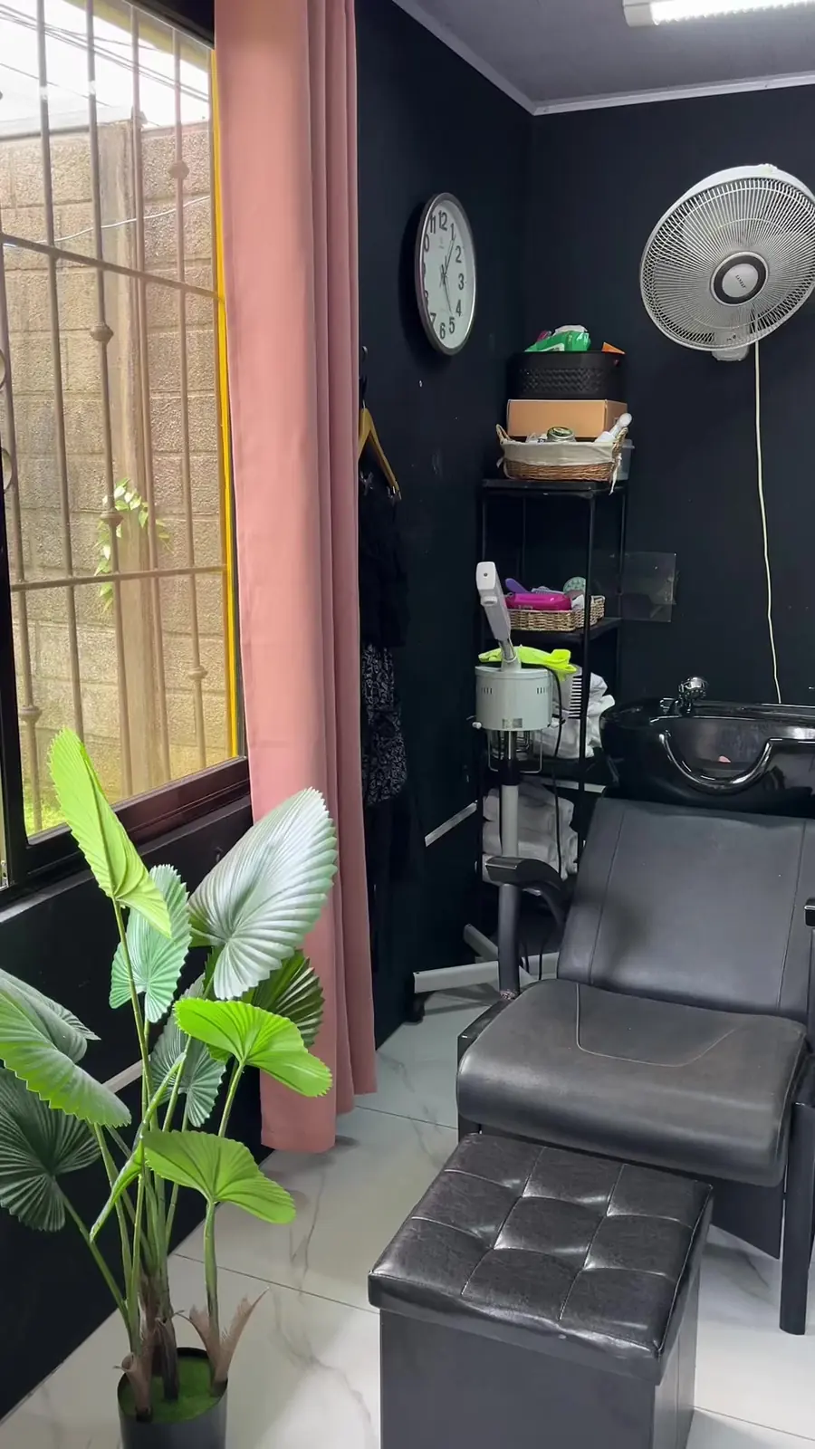Estación de lavado del salón con sillón negro, plantas y cortina rosada
